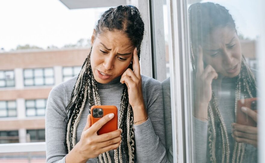 Bekymrad kvinna tittar på mobilen vid ett fönster