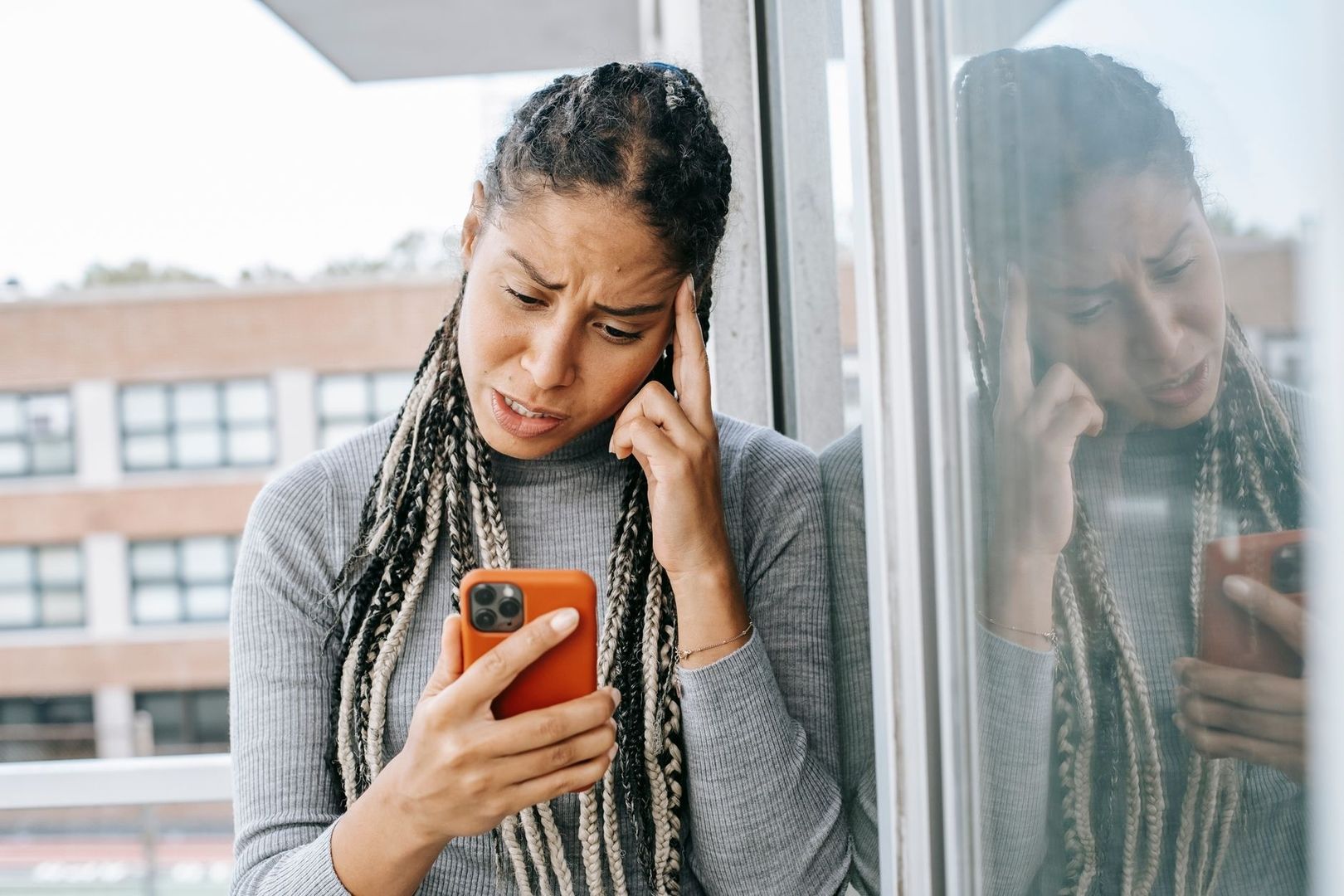 Bekymrad kvinna tittar på mobilen vid ett fönster