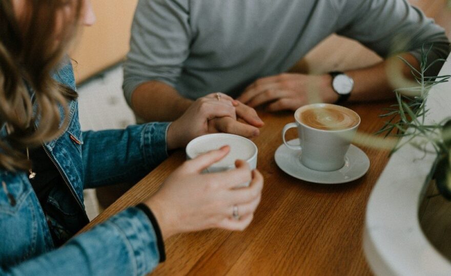 Två personer sitter vid ett cafébord med händerna mötta mellan kaffekoppar