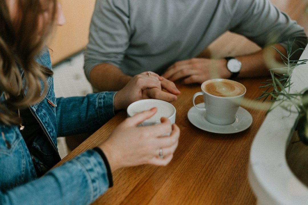 Två personer sitter vid ett cafébord med händerna mötta mellan kaffekoppar